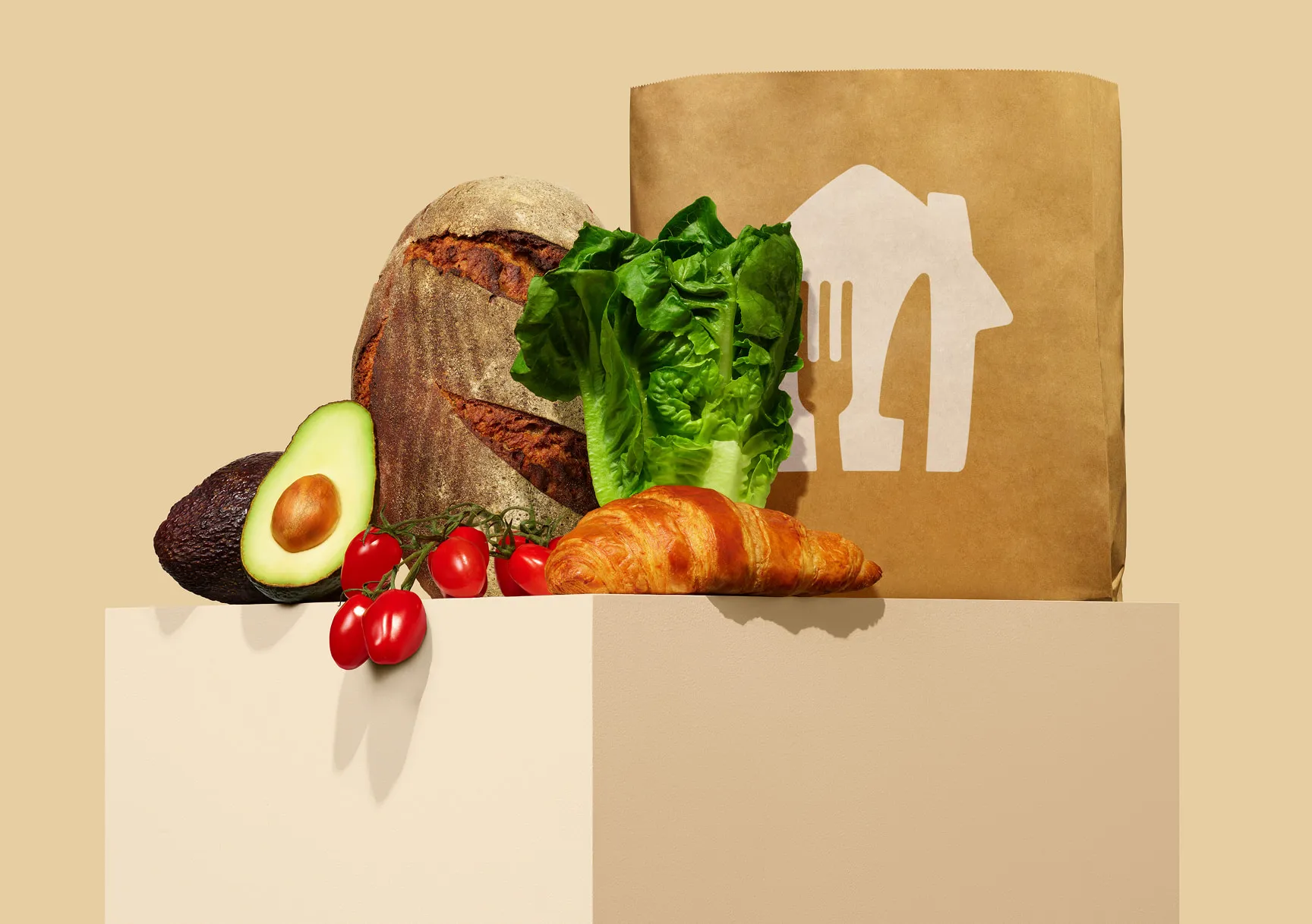 Papierowa torba z logo pyszne.pl, obok świeże warzywa, chleb i croissant na beżowym tle