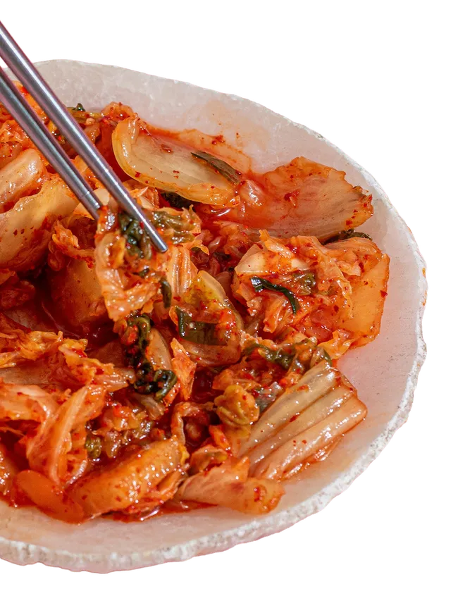kimchi na białym talerzyku, srebrne pałeczki sięgające po nie